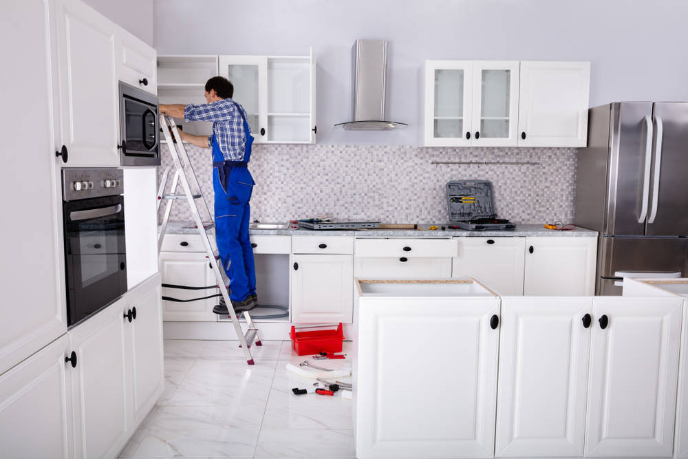 Rear,View,Of,A,Man,Standing,On,Ladder,Adjusting,Cabinet
